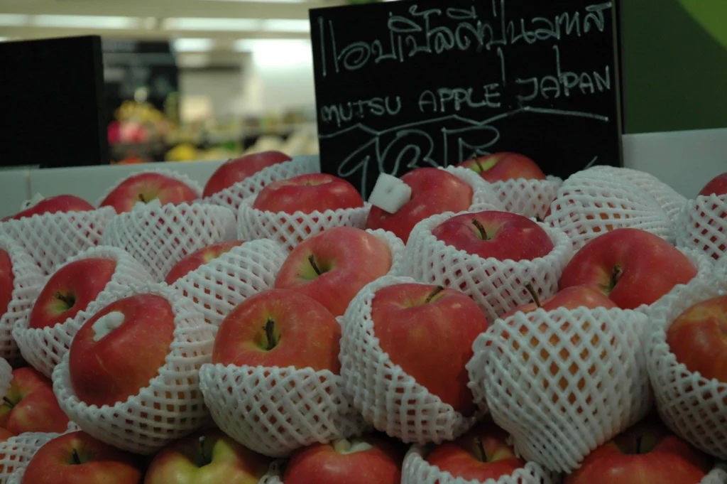 Red Japanese Mutsu apples displayed in protective white foam netting at a market in Thailand.