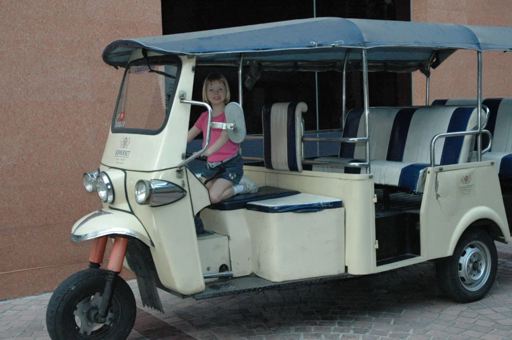 Jessie Rudin as a child sitting in the driver's seat of a traditional tuk-tuk in Thailand.